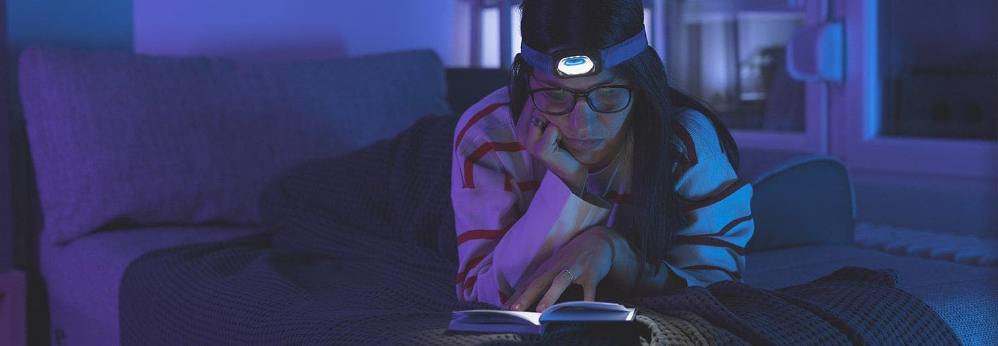 woman with a headlamp on sitting in the dark reading a book