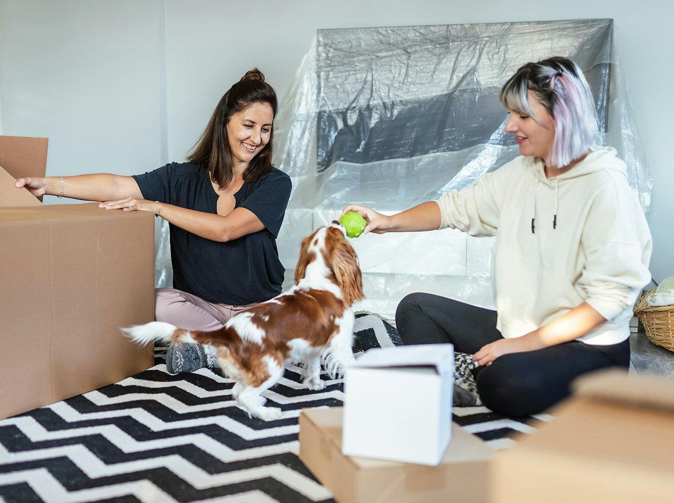 two women unpacking and playing with a dog