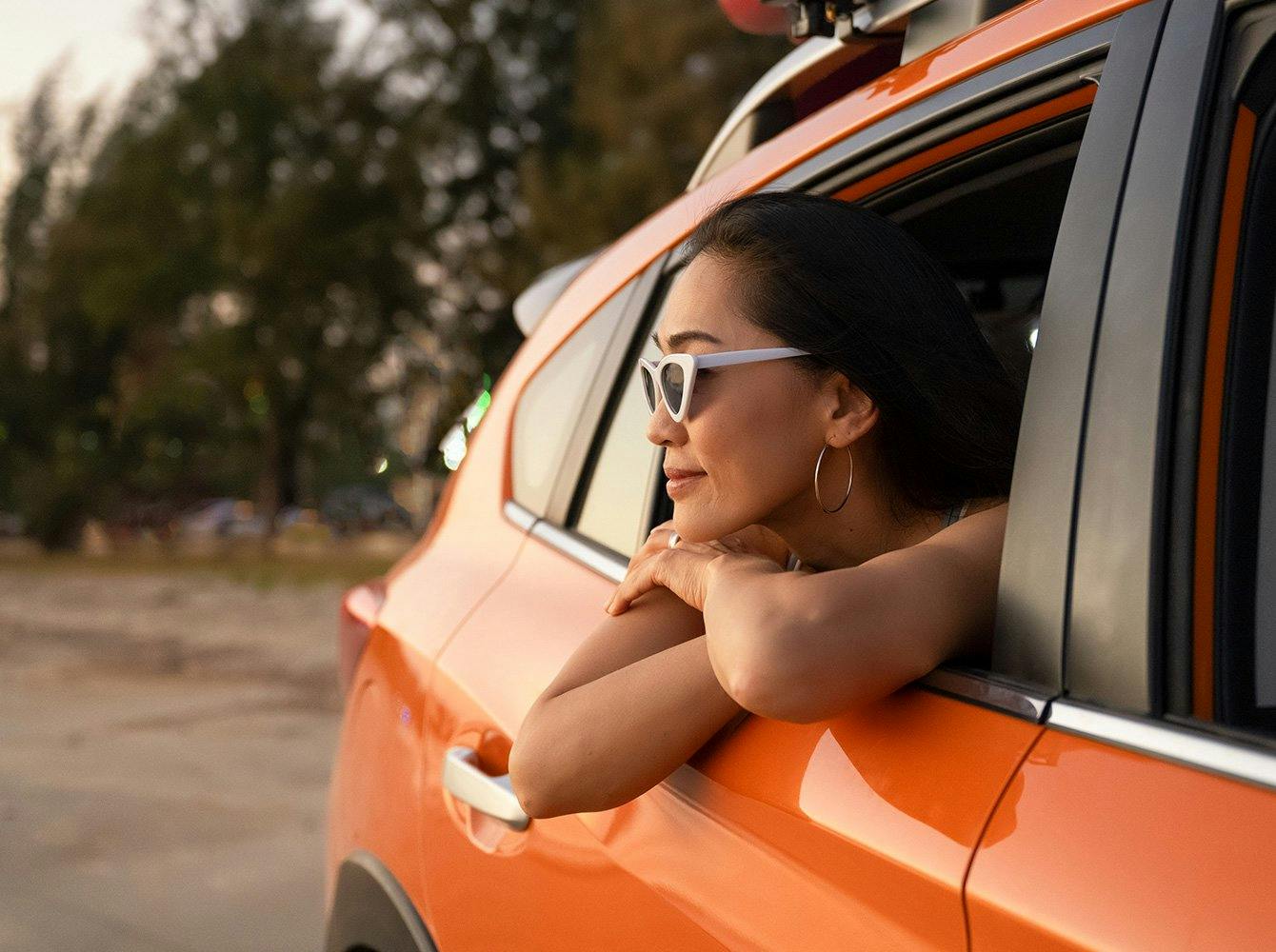 woman with sunglasses on leaning out the rolled down back window of a car