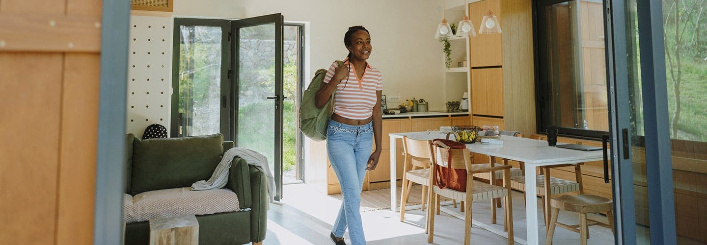 woman with a backpack on her shoulder smiling and walking into an airbnb