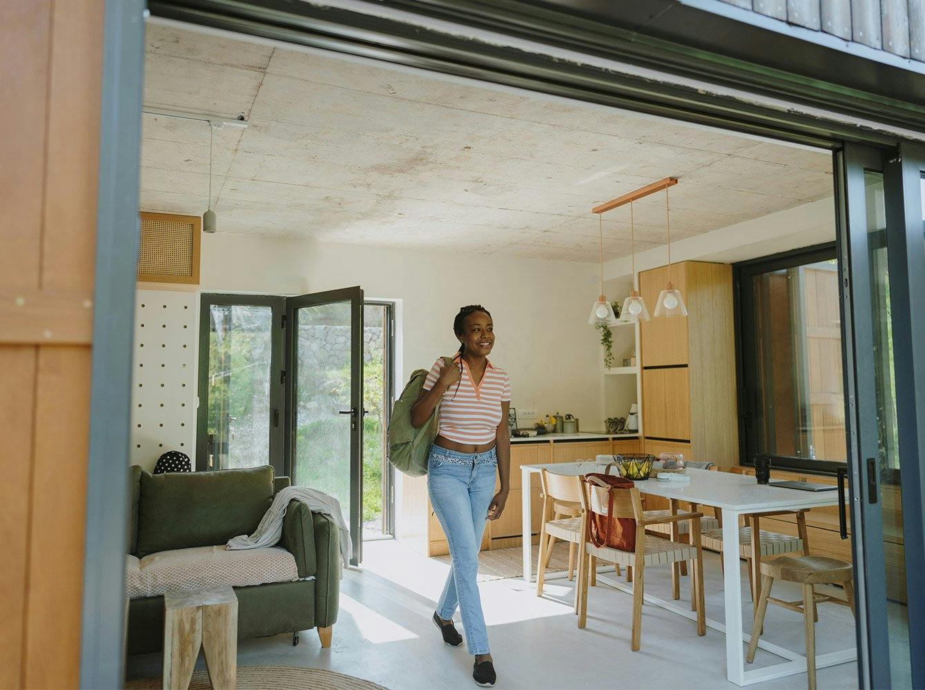 woman with a backpack on her shoulder smiling and walking into an airbnb