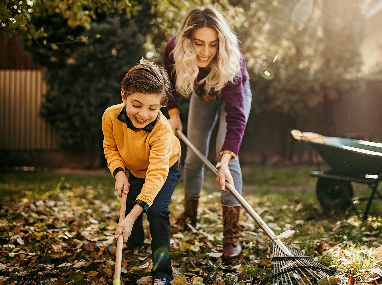 A woman and boy smiling and raking leaves