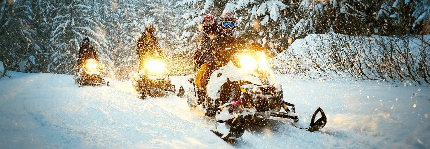 three snowmobiles driving on a trail while snow is falling