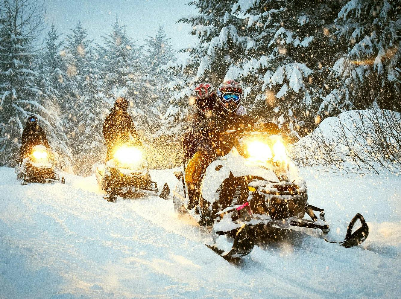 three snowmobiles driving on a trail while snow is falling